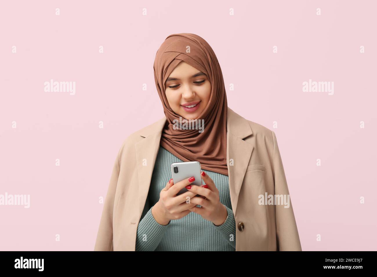 Beautiful young Muslim woman in hijab with mobile phone on pink ...