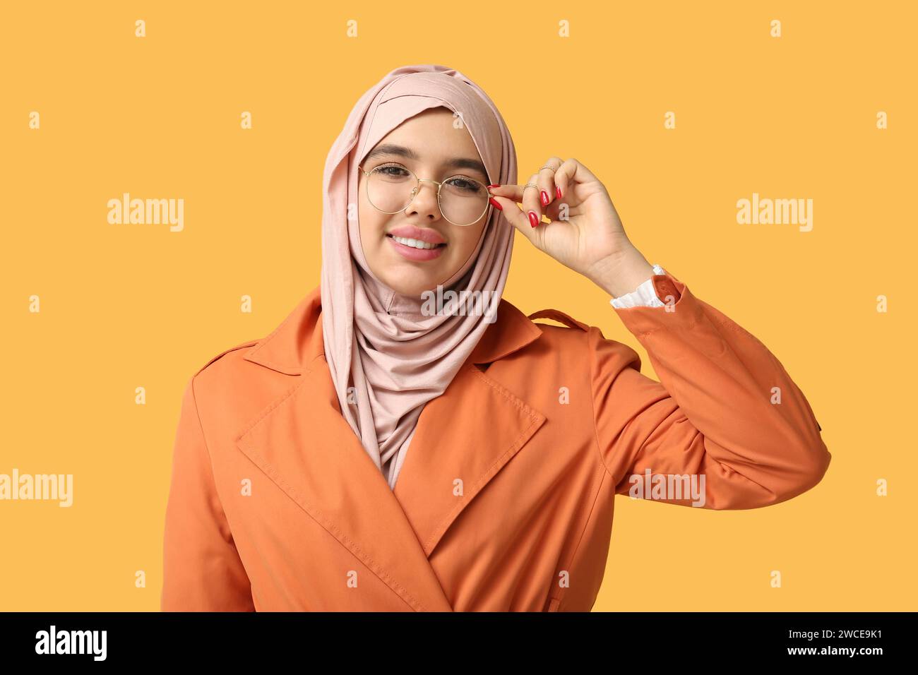 Happy young Muslim woman in hijab and eyeglasses on yellow background ...