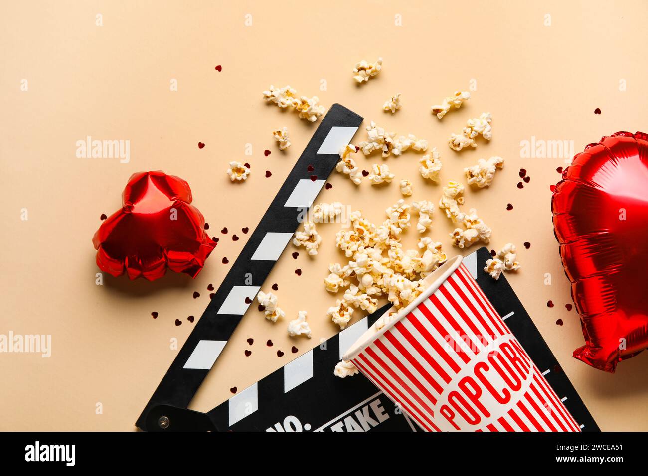 Bucket of popcorn with movie clapper and heart shaped balloons on beige background. Valentine's Day celebration Stock Photo