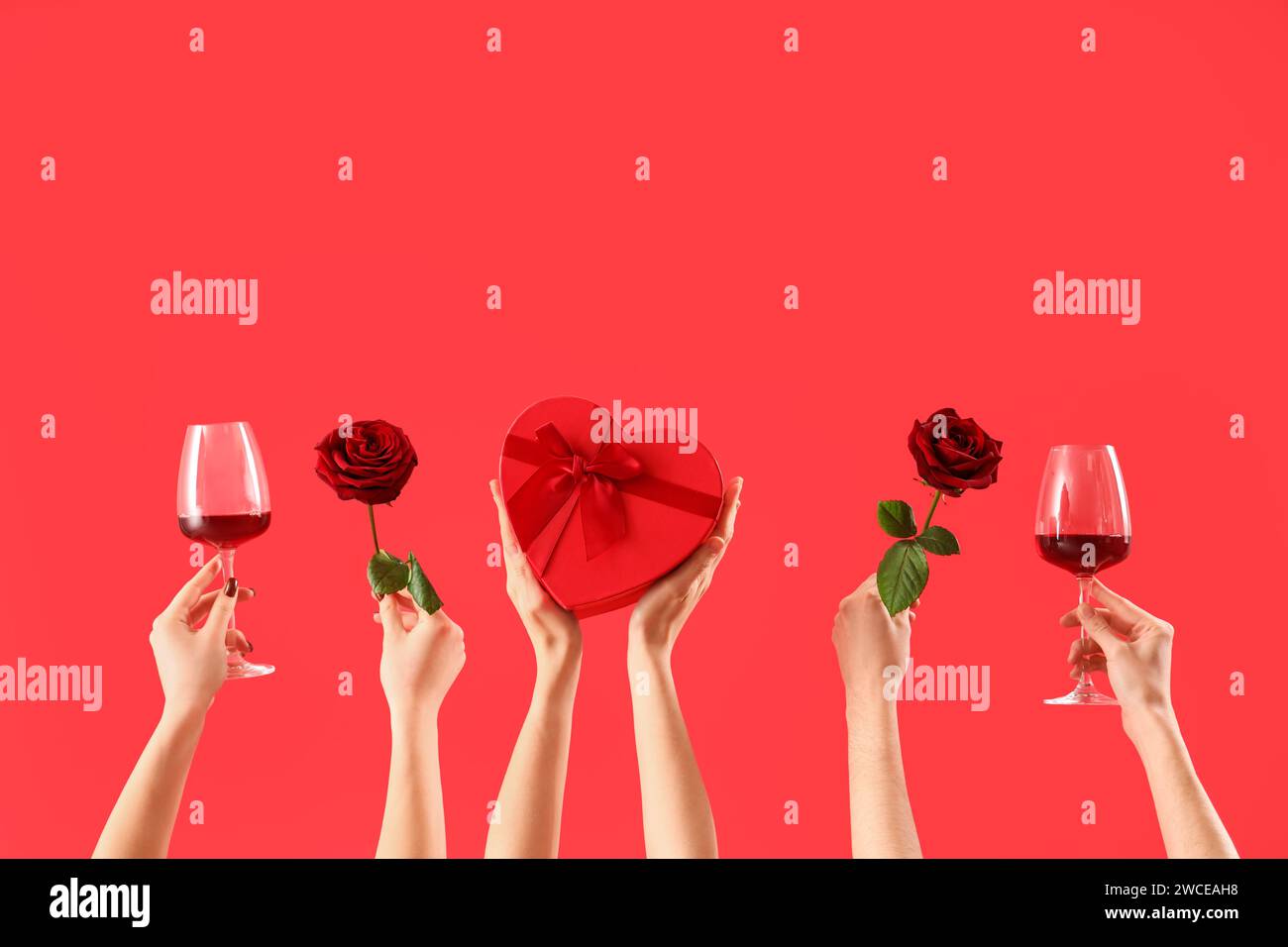 Women with glasses of wine, gift and roses on red background. Valentine ...