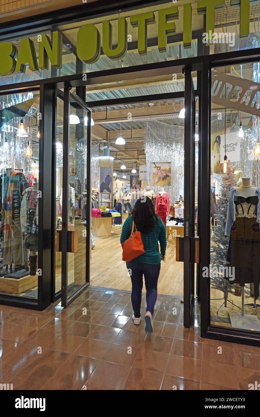 A woman walking into an Urban Outfitters store in a shopping mall - November 2023 Stock Photo