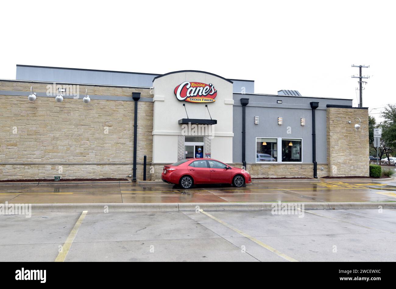 Small red car in the drive thru of a Cane's fast food restaurant on an