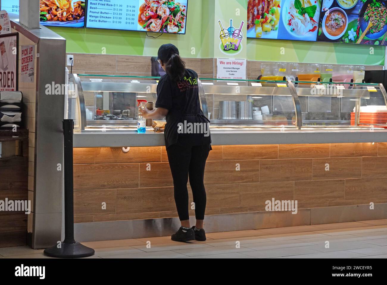 Worker cleaning windows at a Basil Thai restaurant in a food court