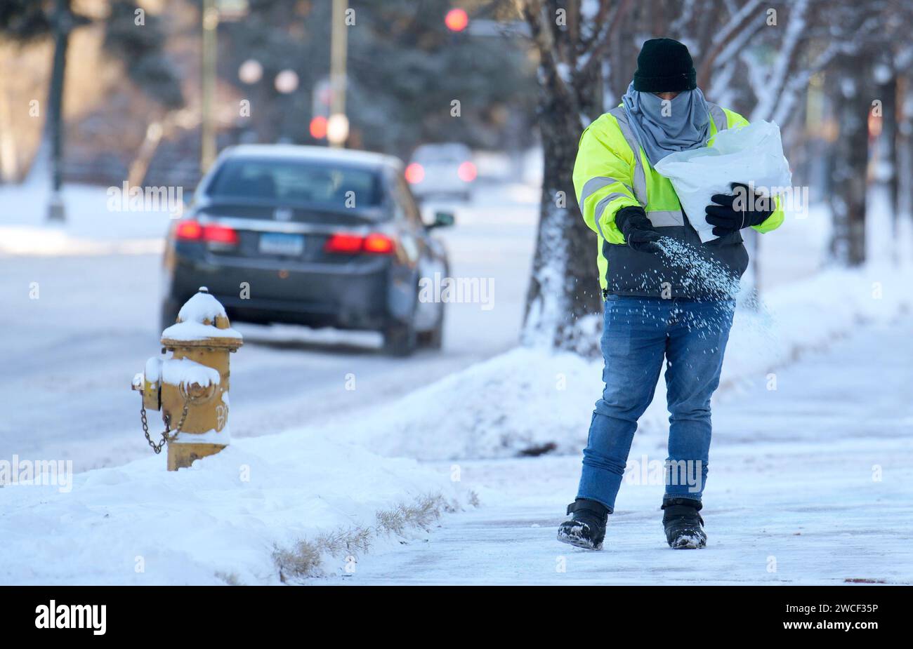 A maintenance worker tosses salt for traction on a sidewalk along Speer ...
