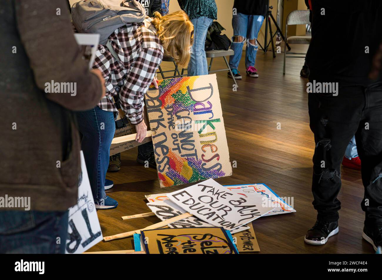 Photo of a woman picking up a 'Darkness Cannot Overcome Darkness' sign from a stack of signs prior to a Martin Luther King, Jr. march event. Stock Photo