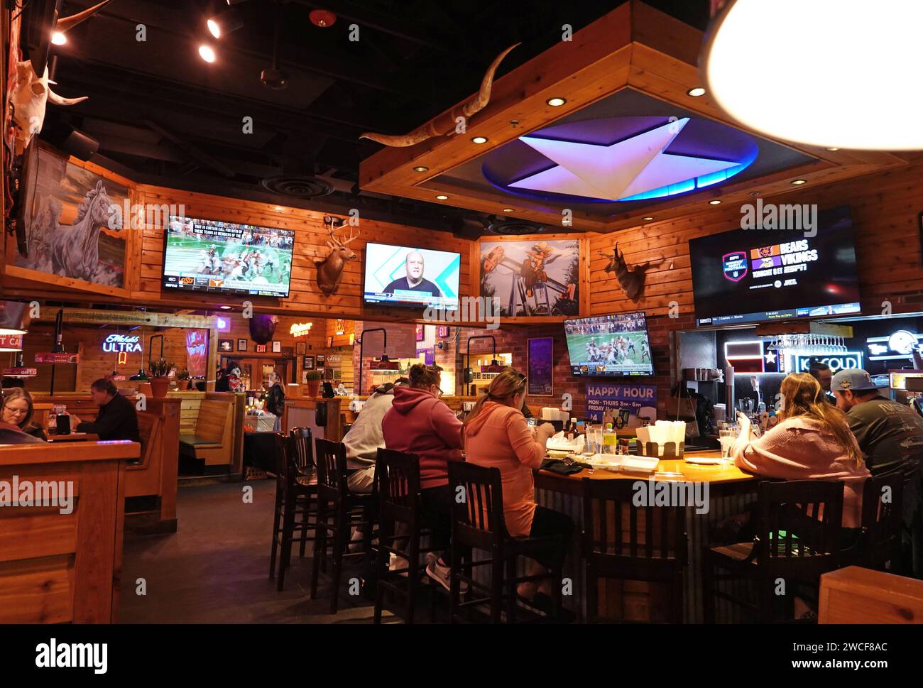 Patrons sit at a bar and watch sports at a Texas Roadhouse restaurant