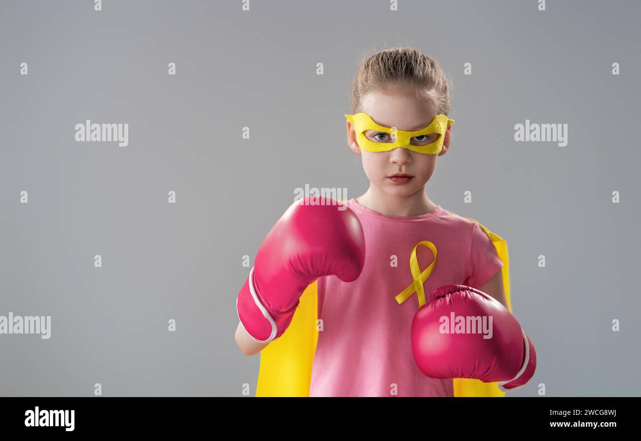 Child in boxing gloves with a yellow ribbon as a symbol of the fight against cancer. Increasing the level of knowledge about kids who have overcome tu Stock Photo