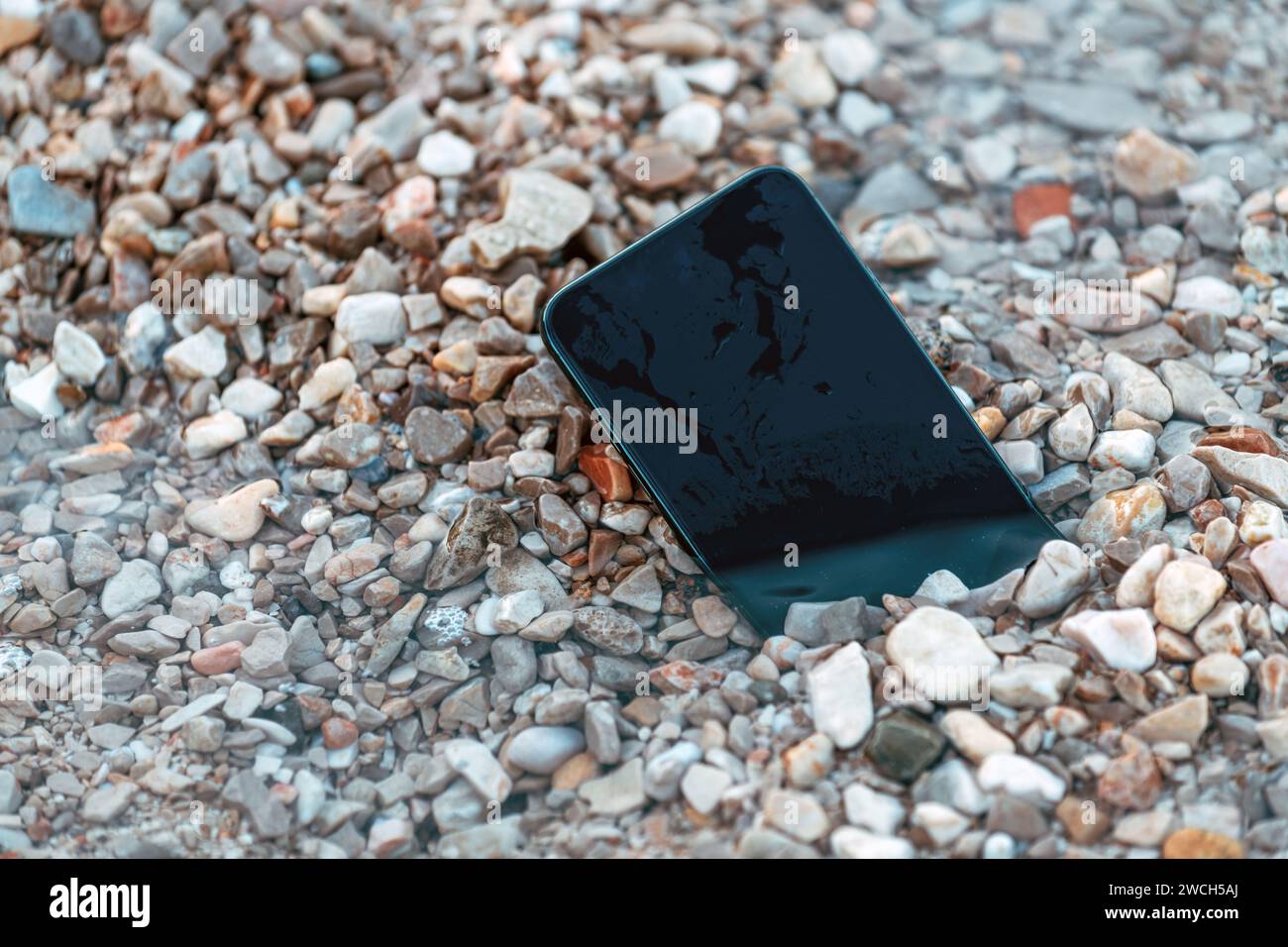 Lost smart phone device in pebbles on seaside beach in summer morning, selective focus Stock Photo