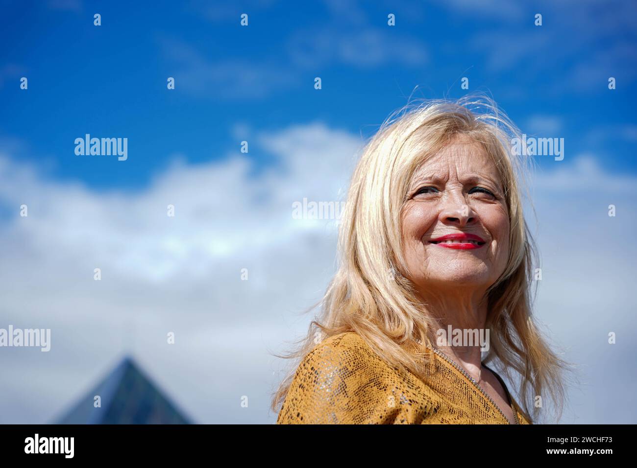 smiling retired woman with blond hair with blue sky in the background Stock Photo