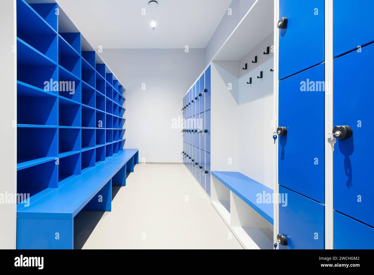 Blue lockers on a wall with key in a lock and cabinet with empty shelves and bench Stock Photo