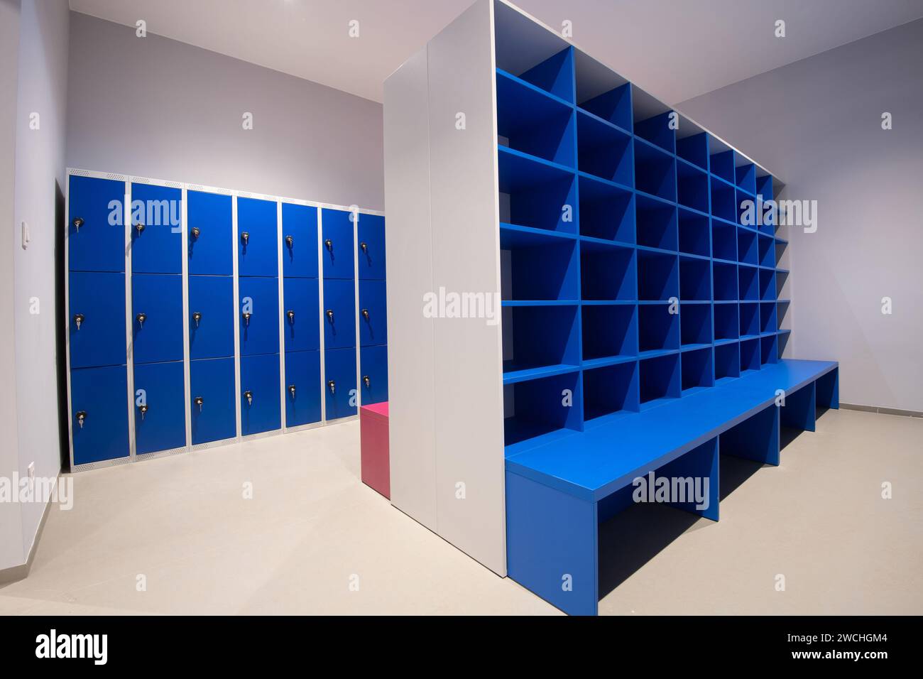 Blue lockers on a wall and cabinet with empty shelves with bench in front Stock Photo