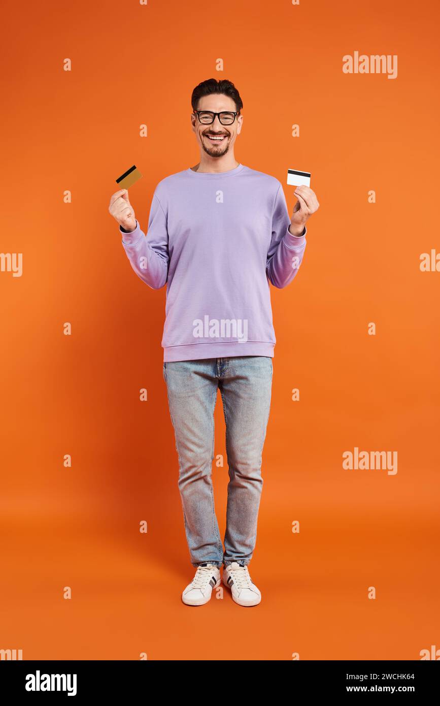 happy bearded man in glasses holding credit cards on orange background, shopping and consumerism Stock Photo