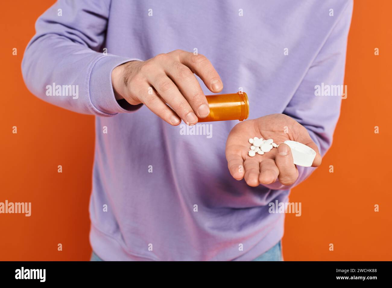 bearded man in purple sweatshirt pouring pills into hand on orange