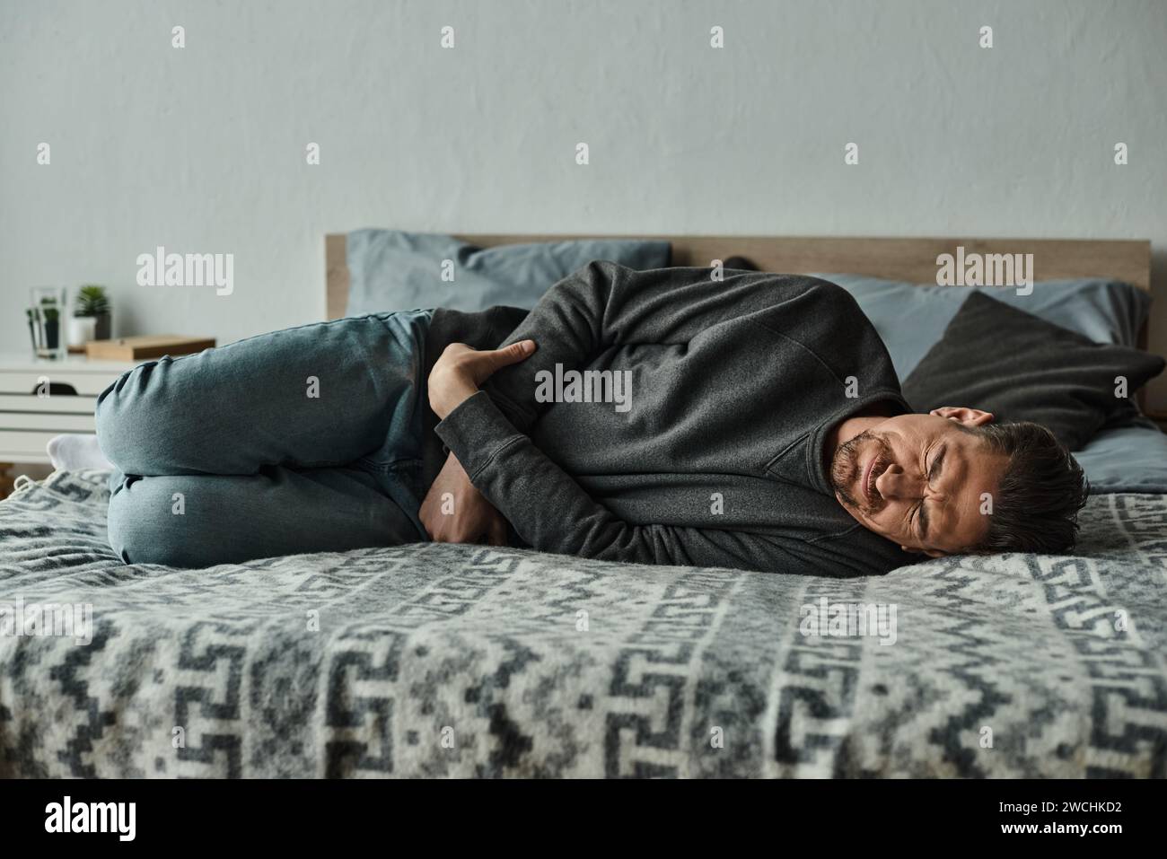 bearded man lying on bed and frowning from pain while suffering from
