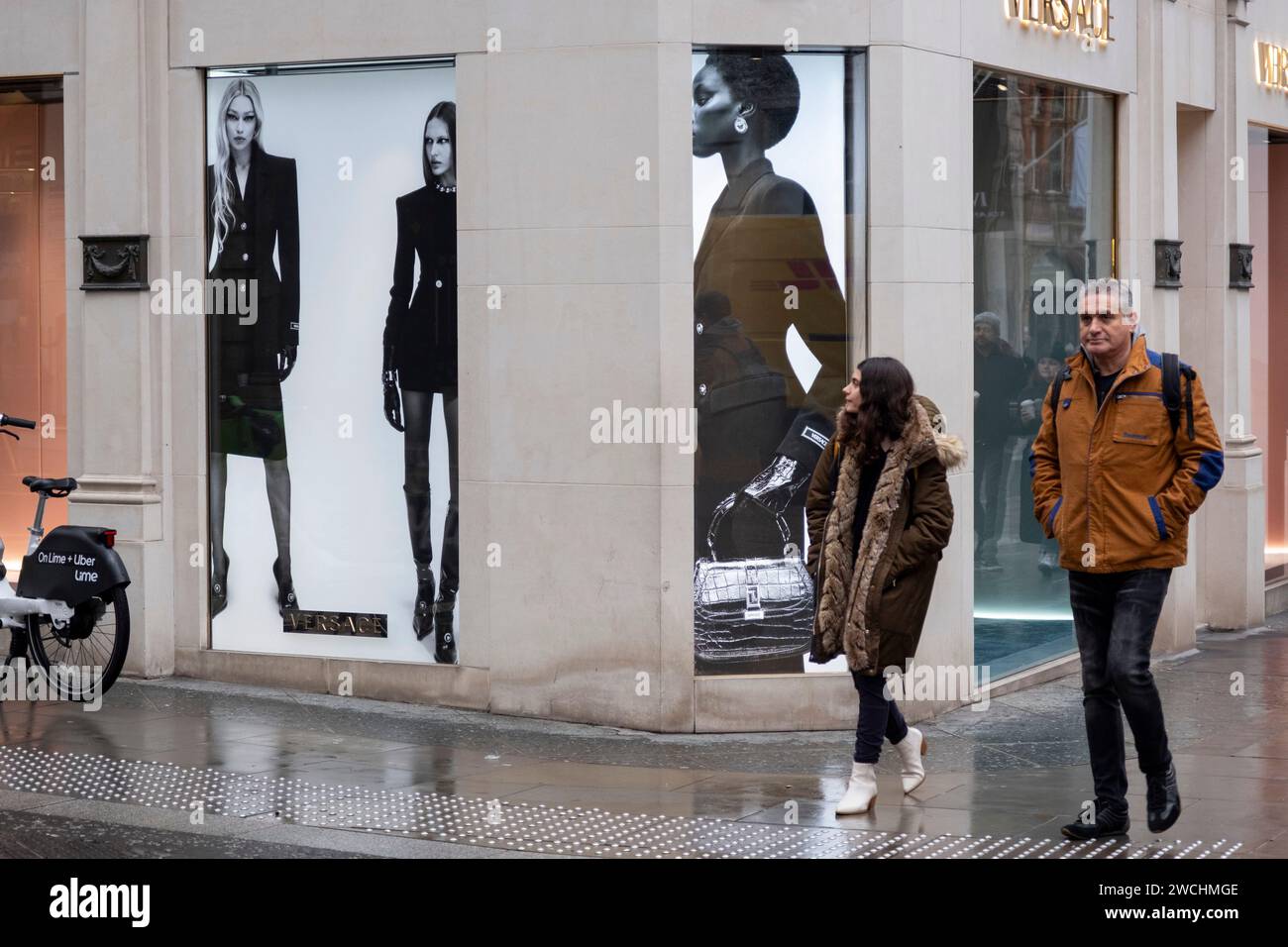 People interact with figures of models outside the Versace store on Bond Street on 4th December 2023 in London, United Kingdom. Bond Street is one of the principal streets in the West End shopping district and is very upmarket. It has been a fashionable shopping street since the 18th century. The rich and wealthy shop here mostly for high end fashion and jewellery. Stock Photo