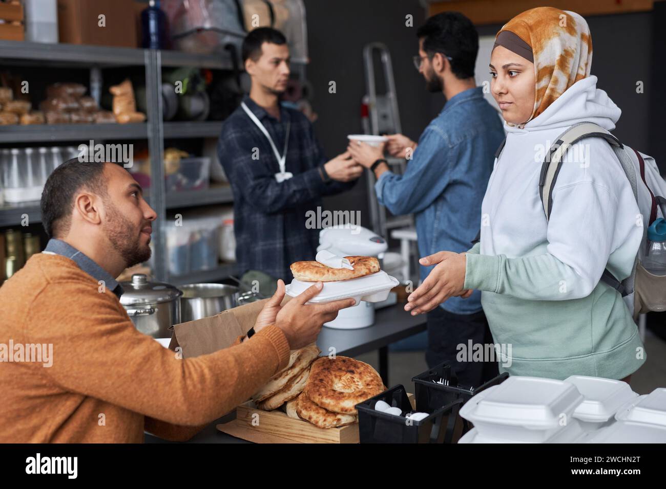 Side view portrait of young Middle Eastern woman wearing headcover receiving free food and donations at refugee help center Stock Photo