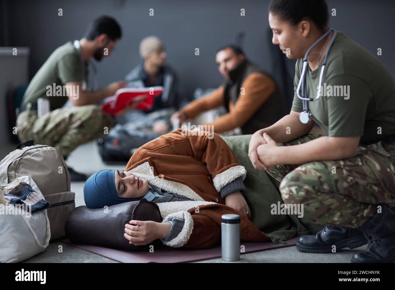 Portrait of Middle Eastern woman lying on floor at refugee shelter and talking to military doctor, copy space Stock Photo