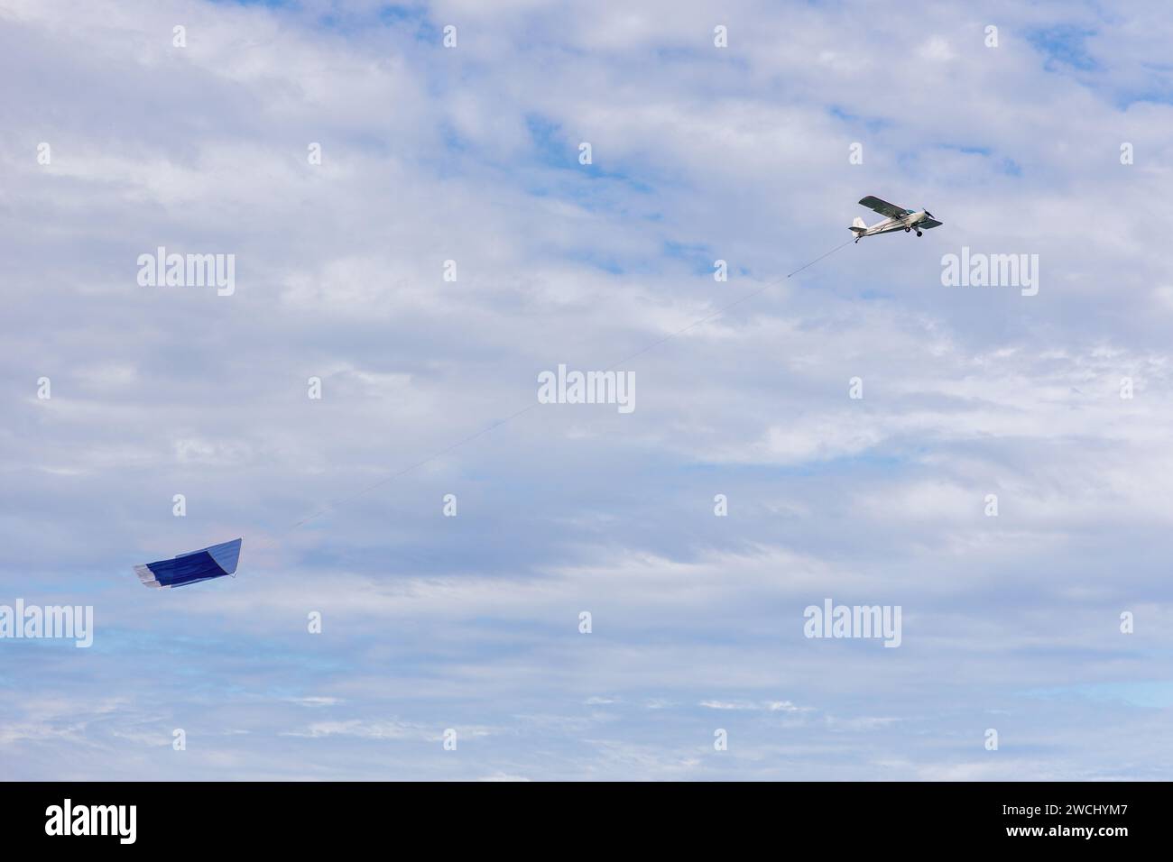 Small plane with blank advertising sign flying over a sky with clouds. Stock Photo