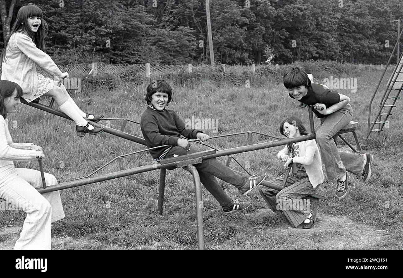 1970s, historical, youngsters playing outside, boys and girls having fun together riding on a metal seesaw at a grassy playground area, England, UK. Despite them being great fun and a healthy activity, See-saws became a less common sight on playgrounds due to overriding safety concerns Stock Photo