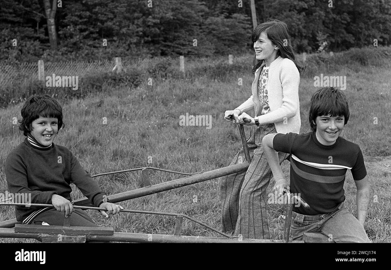 1970s, historical, youngsters playing outside, two boys and a girl having fun together riding on a metal seesaw at a grassy playground, England, UK. Stock Photo