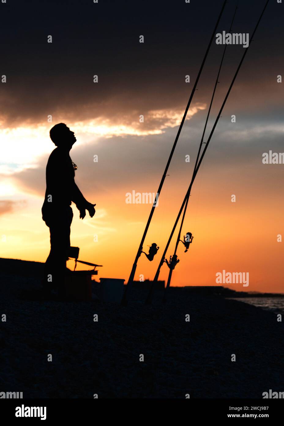 Fisherman cast fishing rods on the seashore at a dramatic sunset ...