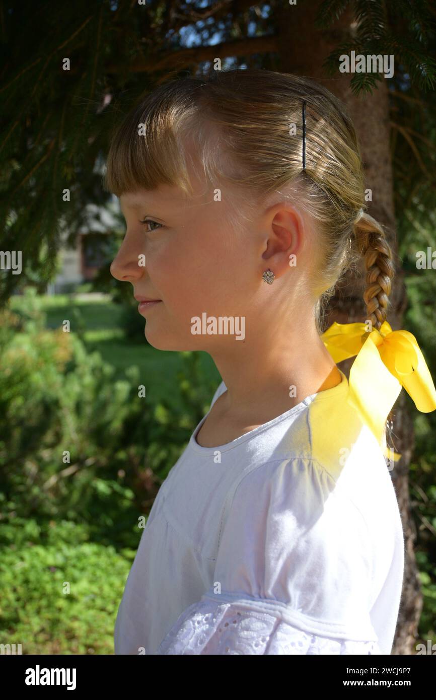 7-year-old girl in a costume and braided braid with a yellow bow, photographed from the profile. Stock Photo