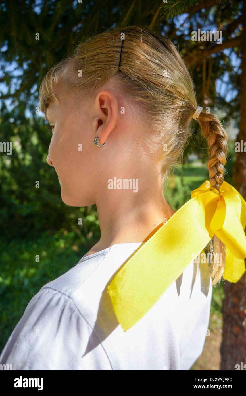 7-year-old girl in a costume and braided braid with a yellow bow, photographed from the profile. Stock Photo