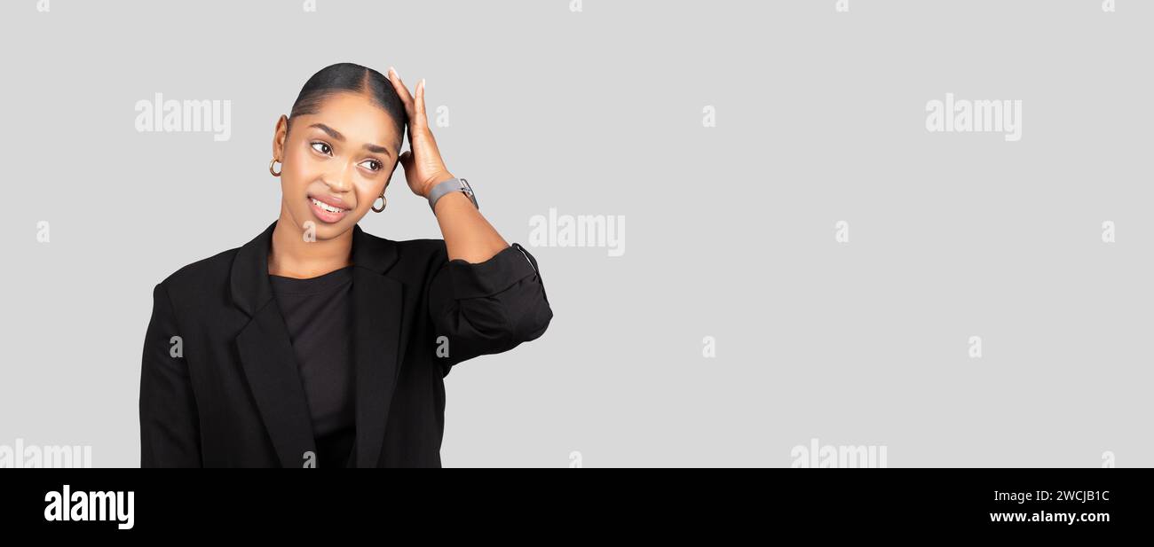 A professional young woman in a black blazer looks surprised, hand on head Stock Photo