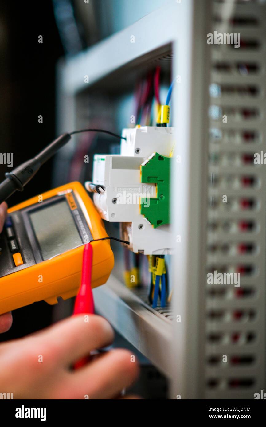 an electrician working in an electrical cabinet as Tests cables using a Tester. Stock Photo