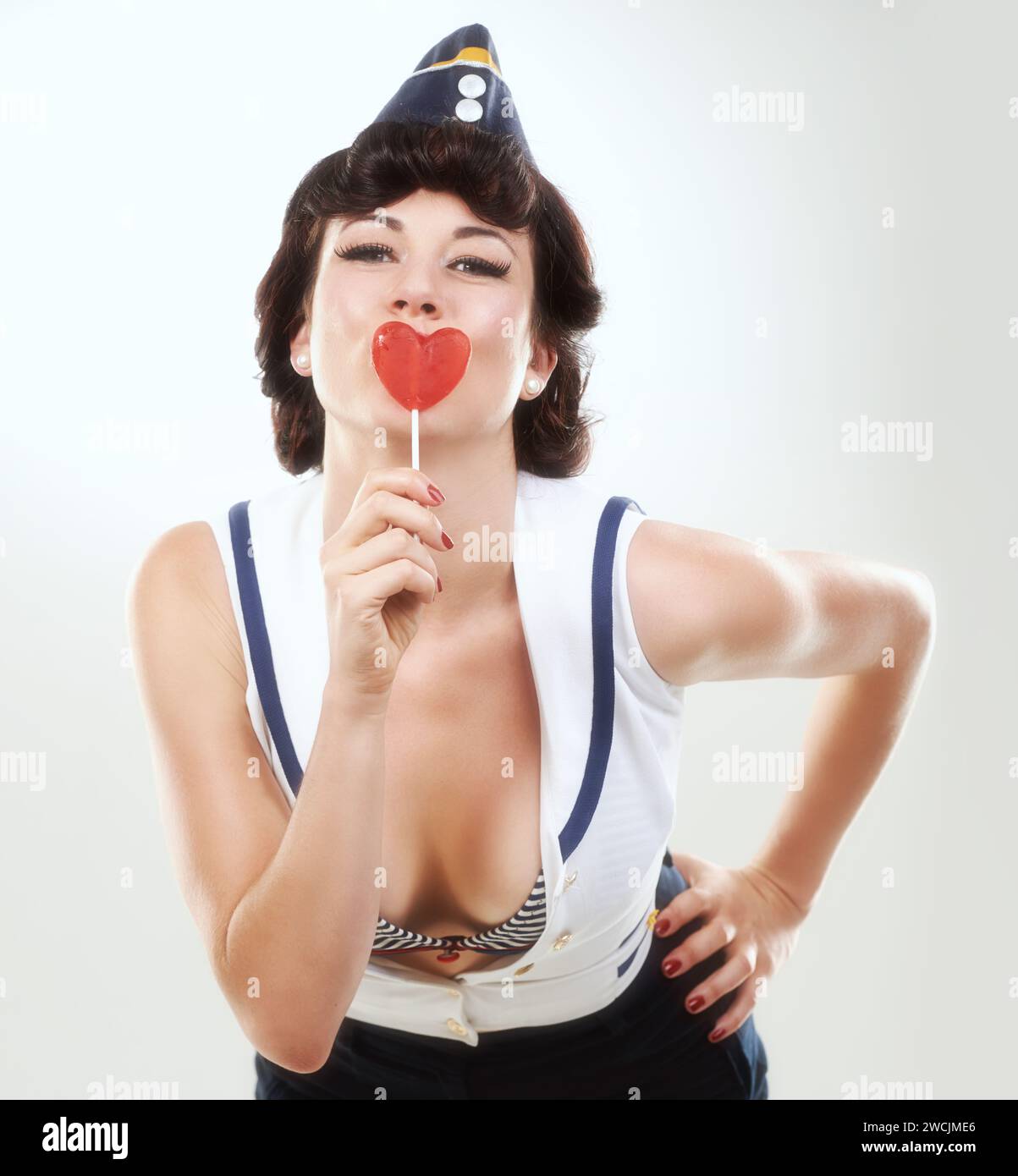 Portrait, pinup and sailor woman with lollipop in studio isolated on a white background. Face, candy sweets and air hostess with confectionery snack Stock Photo