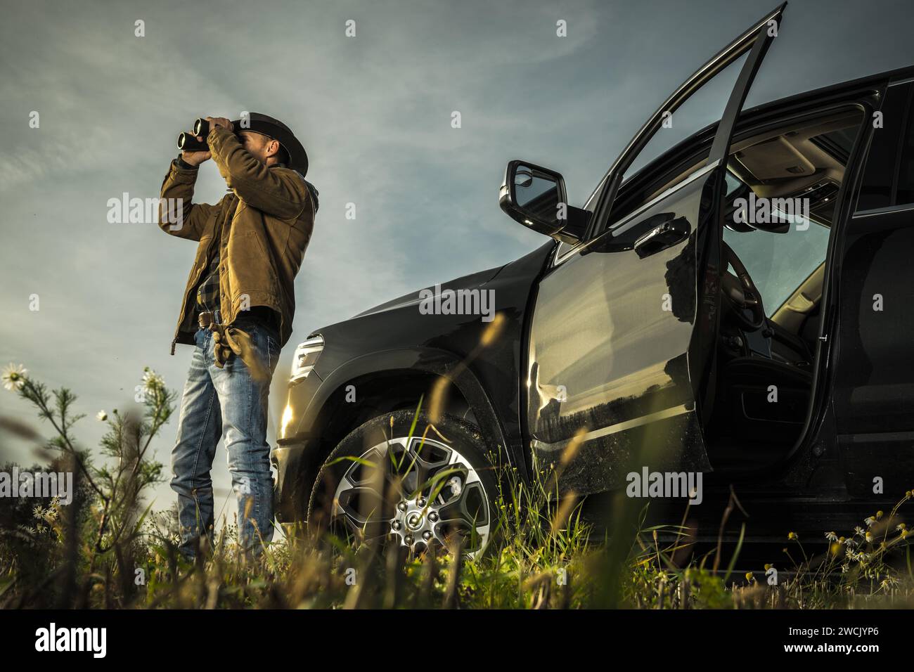 Caucasian Land Owner Staying Next to His Pickup Truck and Spotting Wildlife on His Ranch Using Binoculars Stock Photo