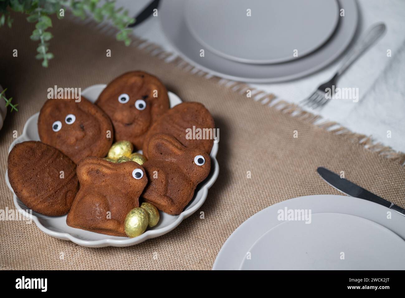 Close-up of Easter muffins shaped as bunnies and eggs with eyes, chocolate eggs on served table setting Stock Photo