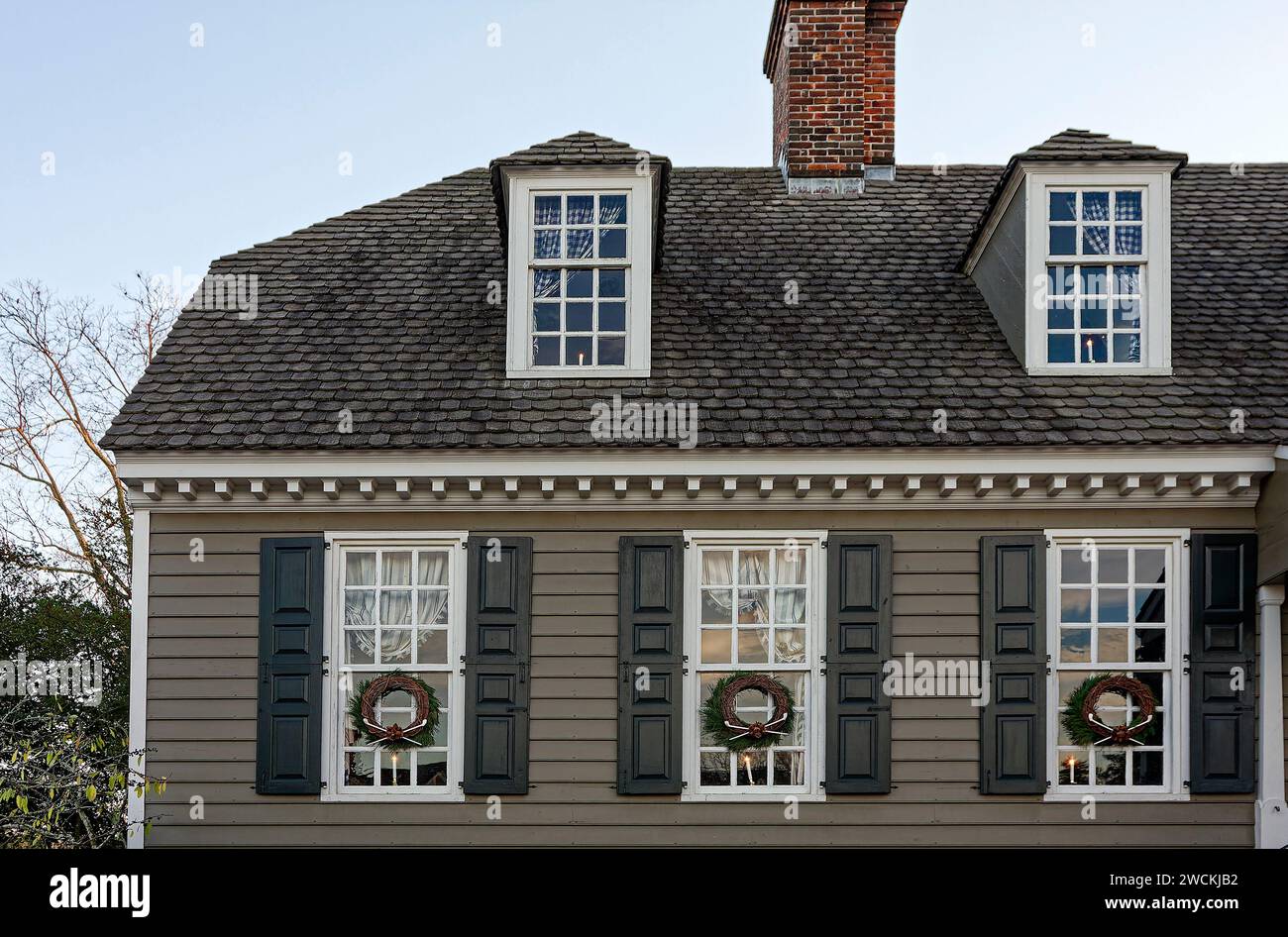 colonial house, 3 windows with shutters, 2 dormer windows, Christmas decorations; lighted candles, 3 wreaths, brick chimney, old, dusk, Virginia; Will Stock Photo