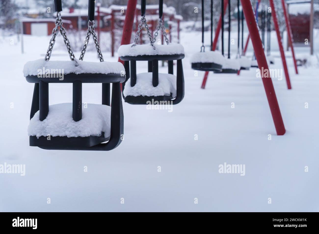 Close up of swings covered in snow at the empty playground in winter. Finland. Stock Photo