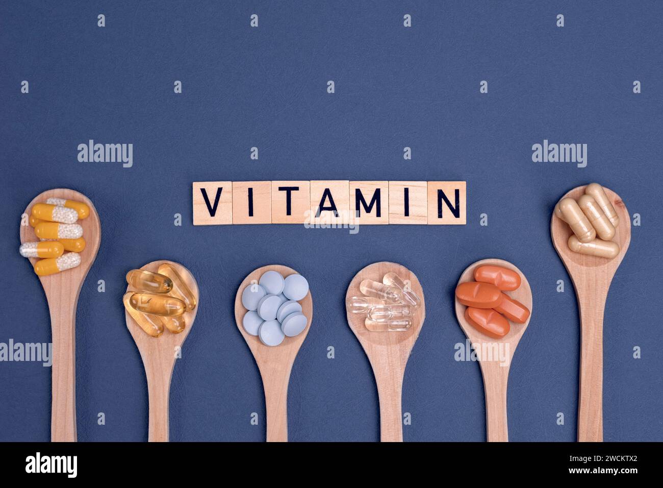 Different vitamins in wooden spoons with text on gray background. Pills, drugs, supplements, medicine, pharmacy and healthcare concept. Stock Photo