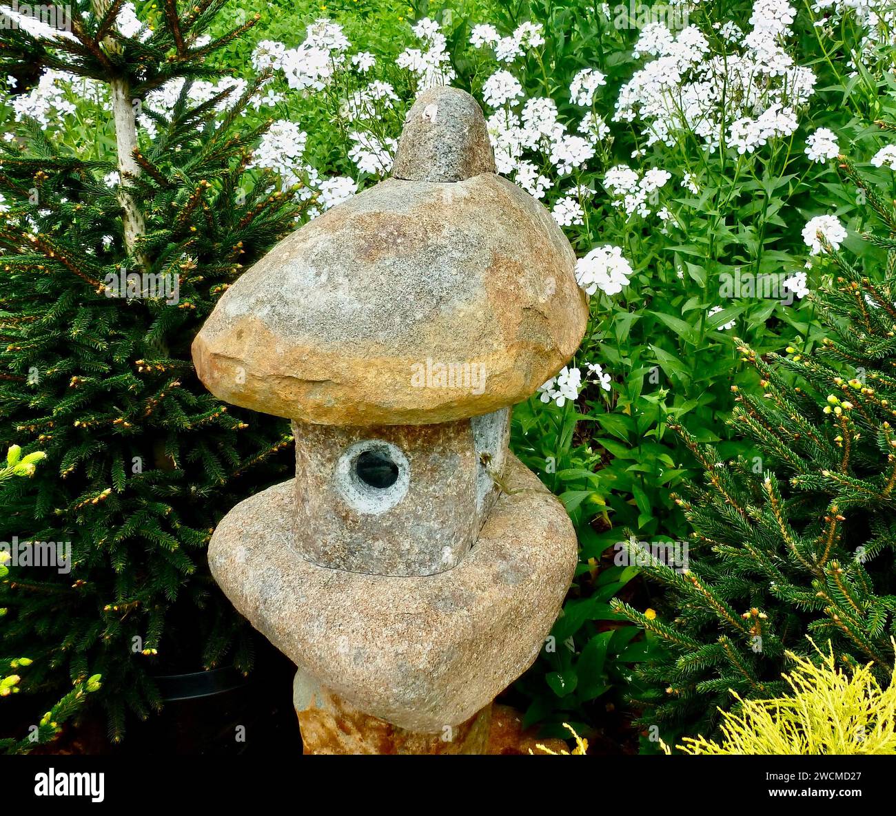 Stone lantern with white flowers, rock backdrop Stock Photo