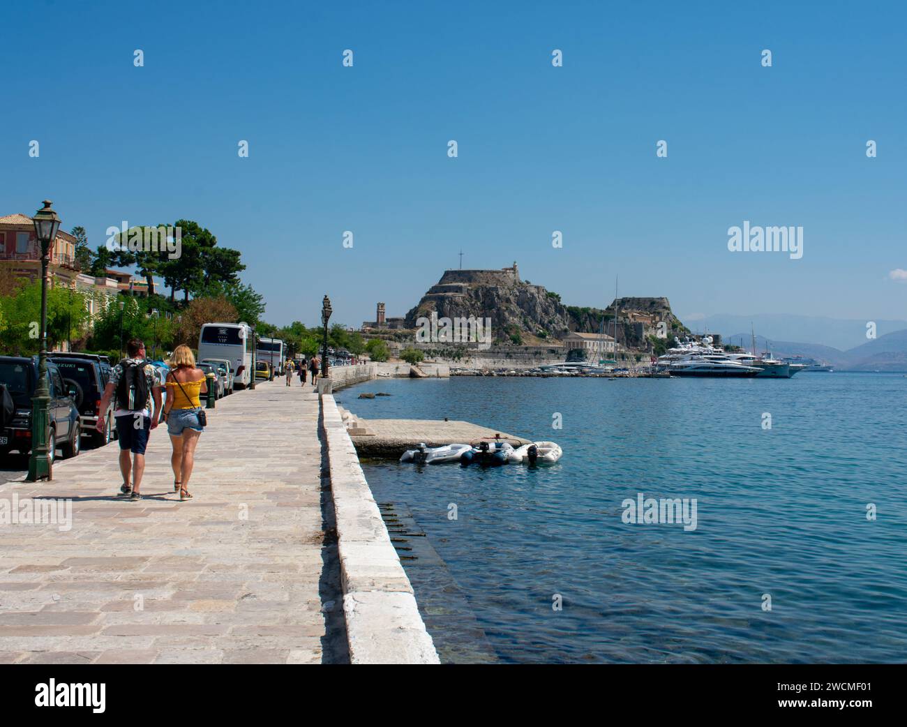 Couple of tourists visiting corfu island walking along the promenade with views to the sea and old fortress Stock Photo