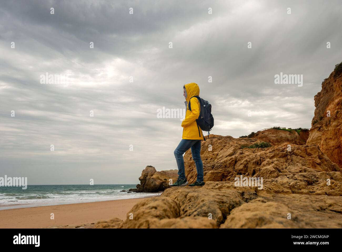 mid adult female walker standing on rocks and looking at coastal view on gloomy day Stock Photo