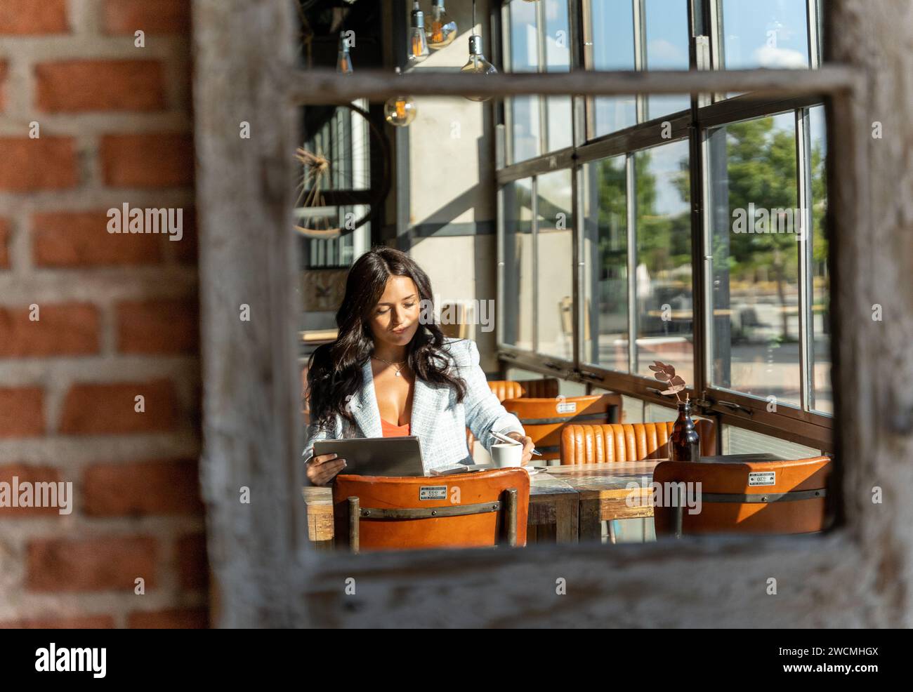 Reflection in the mirror of a woman using a digital tablet while sitting in a coffee shop. Technology concept. Stock Photo