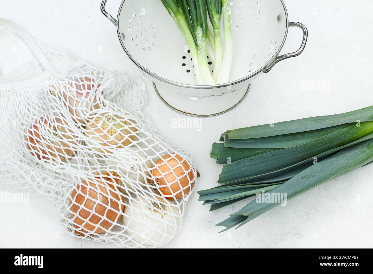 Colander and string bag with different kinds of onion on white ...