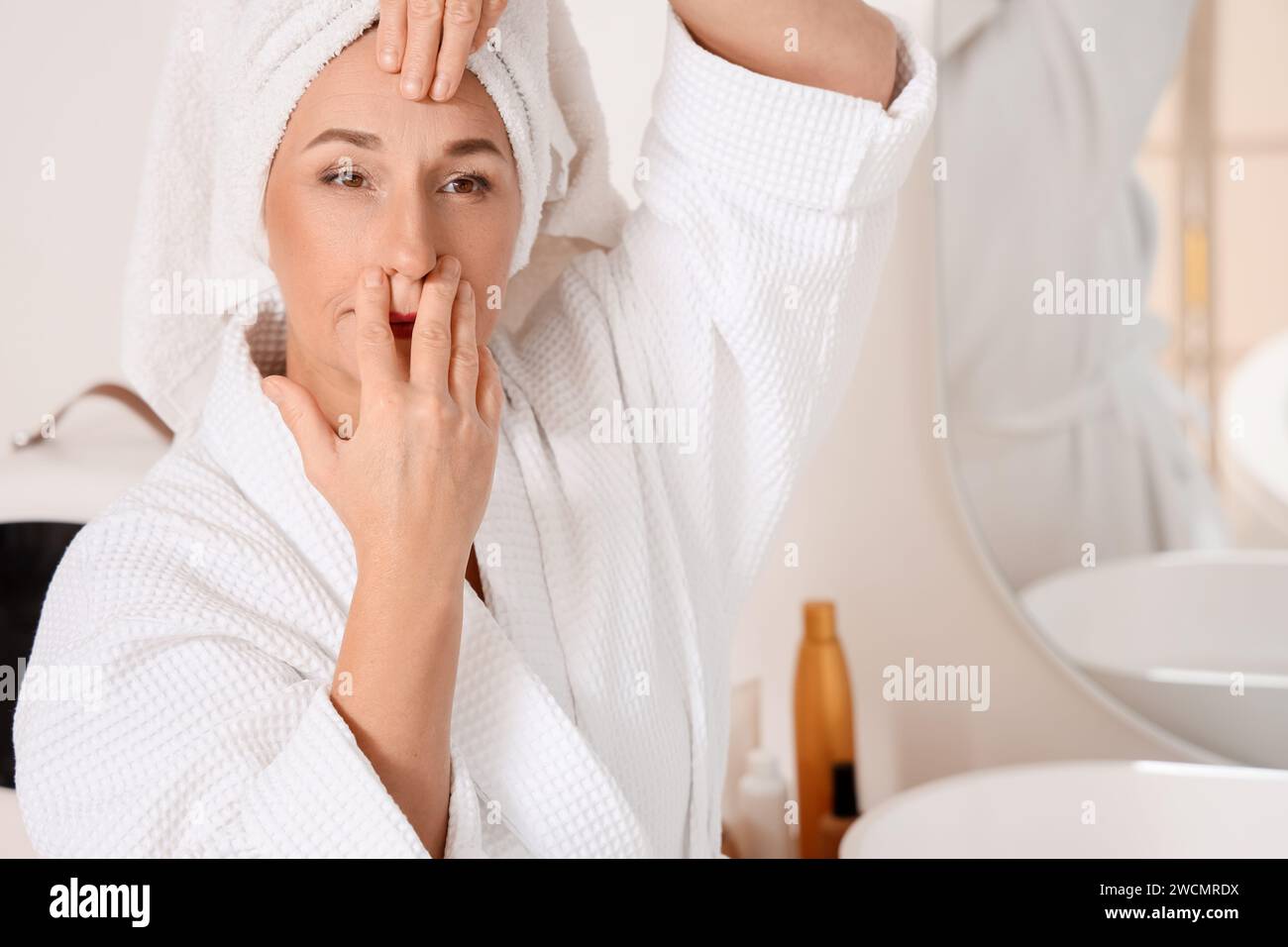 Mature woman doing face building exercise after shower in bathroom
