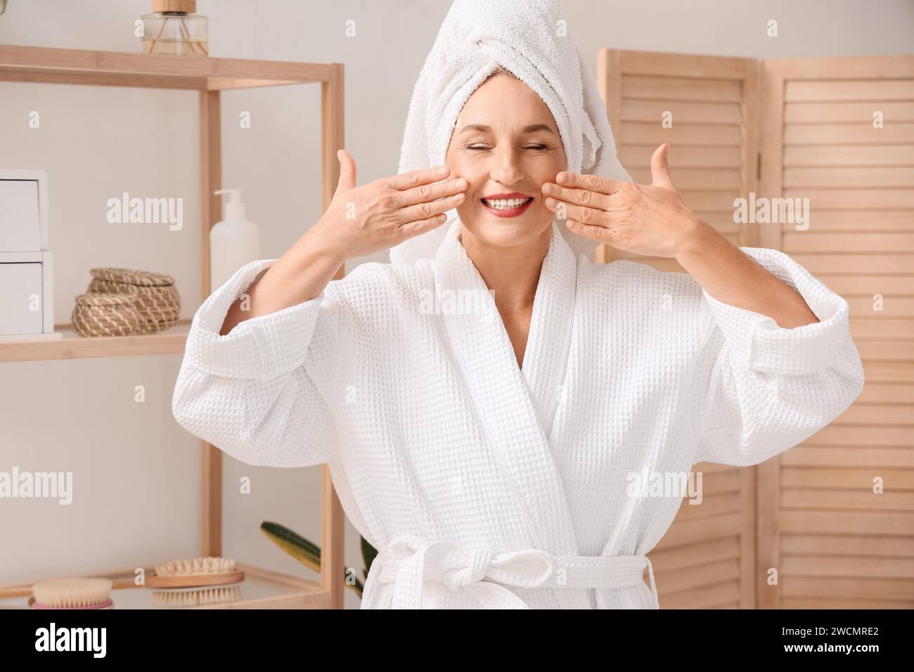 Mature woman doing face building exercise after shower in bathroom