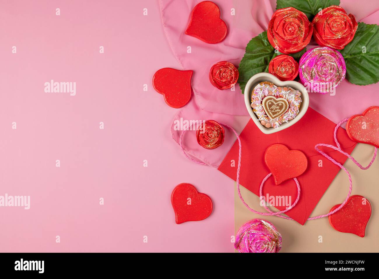 An arrangement of decorative hearts, roses and an envelope, heart-shaped cupcake, ideal for Valentine's Day, on a pink background Stock Photo
