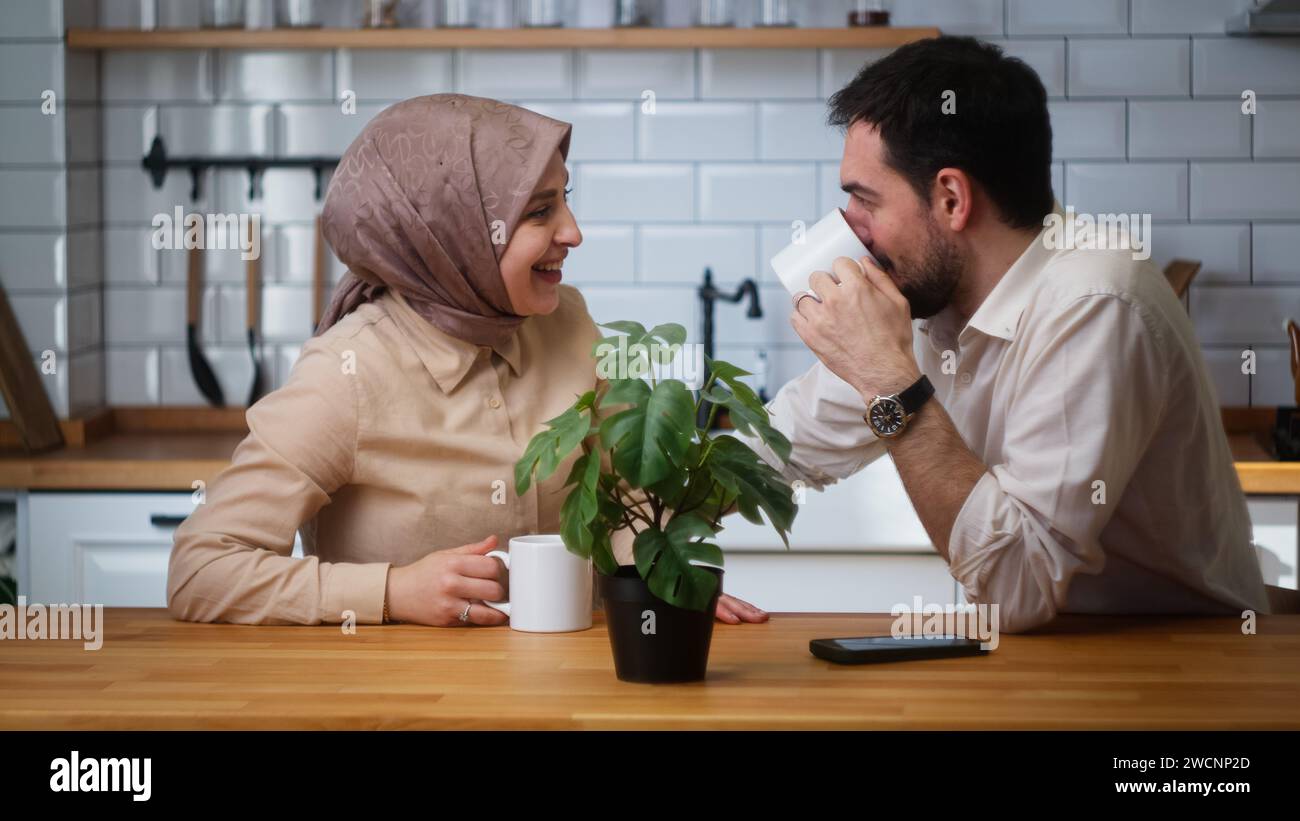 Smiling married couple sitting in the kitchen drinking coffee from a mug and having a pleasant conversation Stock Photo