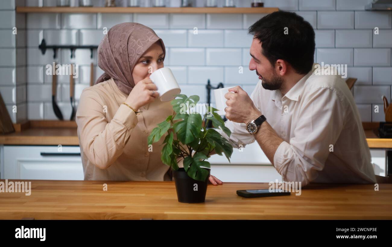 Young married couple sitting in the kitchen drinking coffee from a mug and having a pleasant conversation Stock Photo