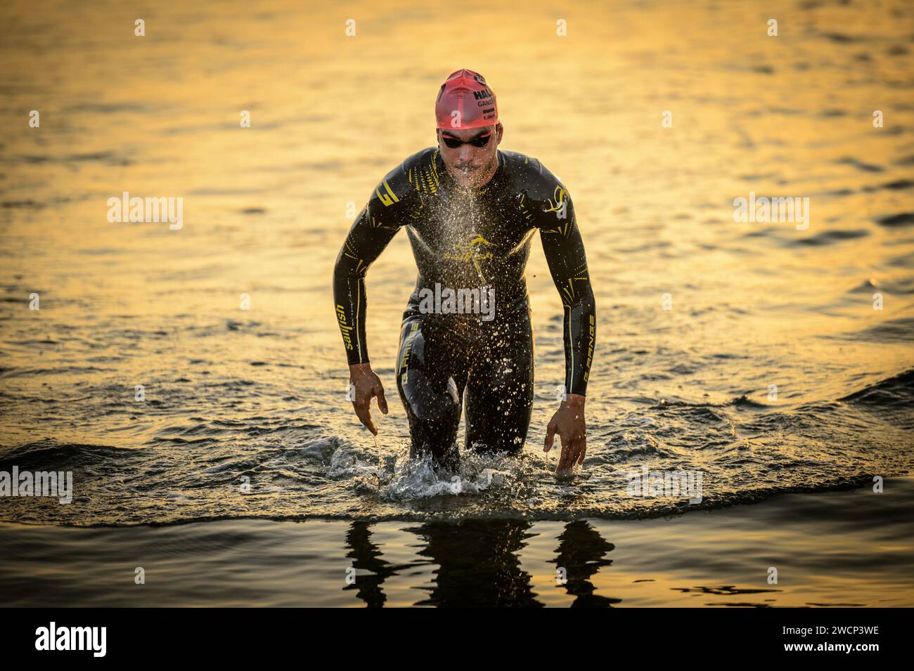 First place triathlete exiting the water in a wetsuit blowing during a beautiful sunrise to switch to the cycling sector in Gandia, Valencia, Spain Stock Photo