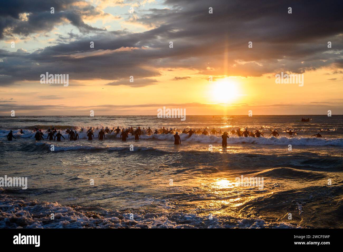 Triathletes in wetsuits running into the sea during a beautiful sunrise to start the competition in Burriana, Castellon, Spain Stock Photo