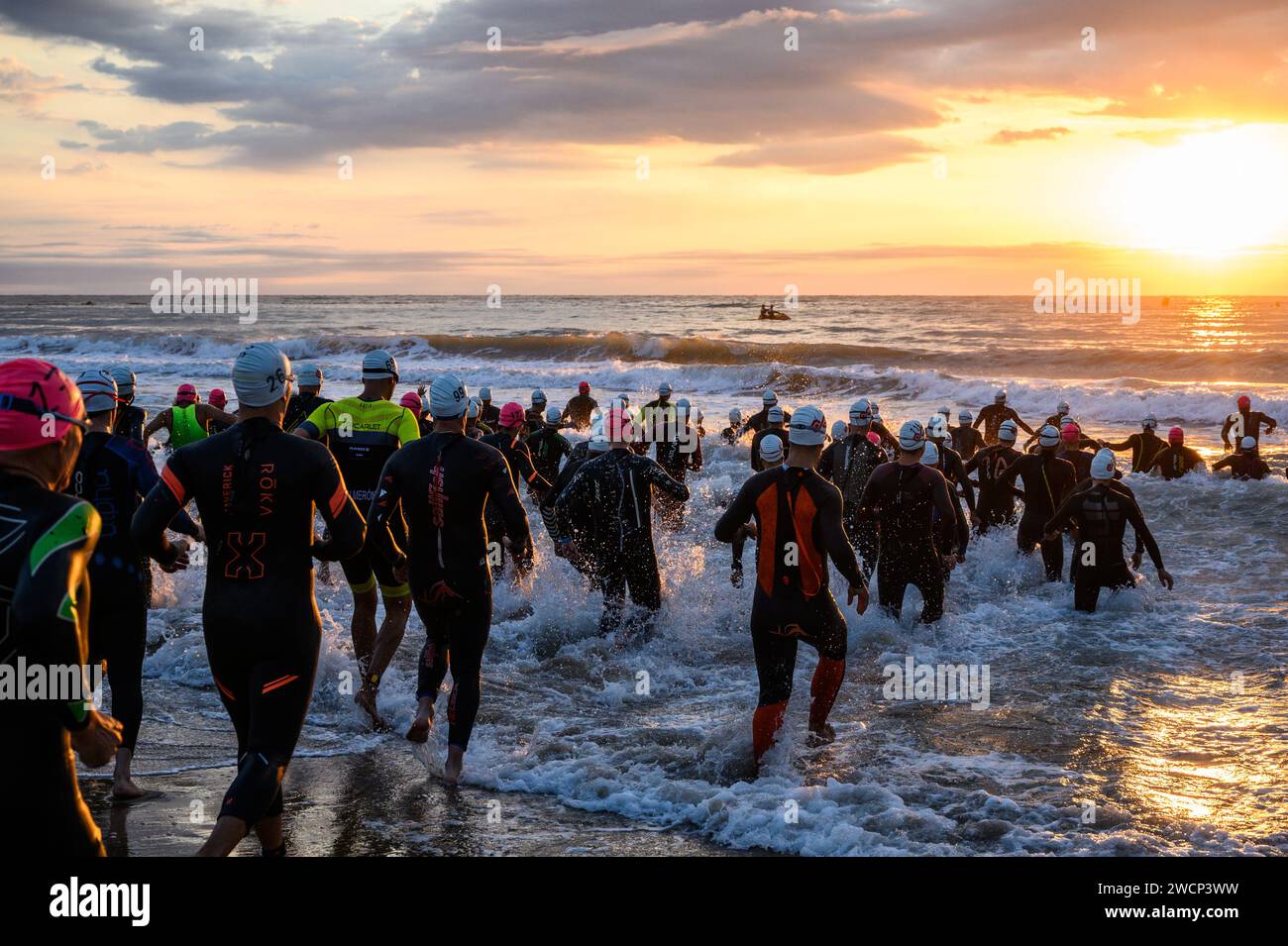 Triathletes in wetsuits running into the sea during a beautiful sunrise to start the competition in Burriana, Castellon, Spain Stock Photo