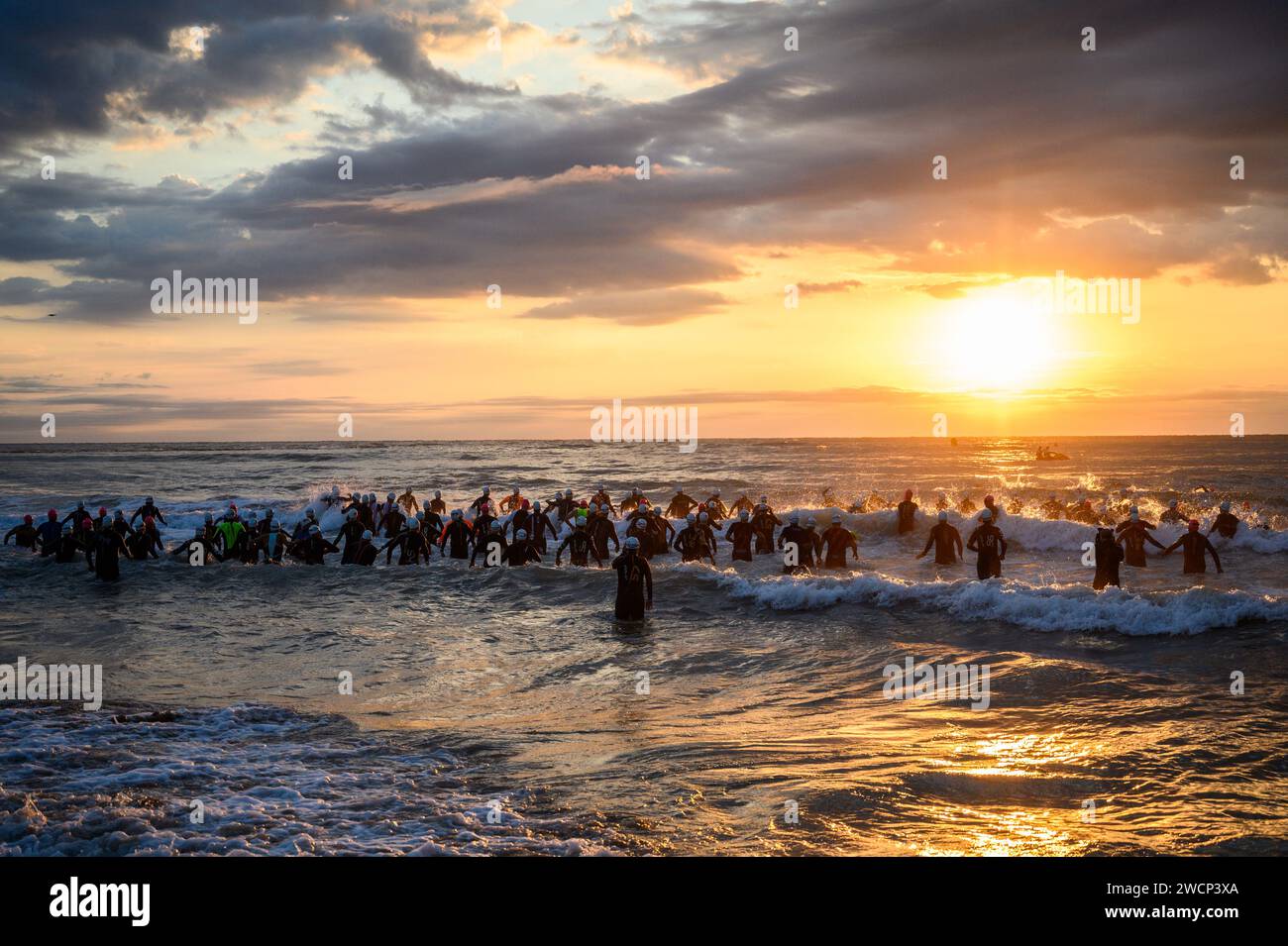 Triathletes in wetsuits running into the sea during a beautiful sunrise to start the competition in Burriana, Castellon, Spain Stock Photo
