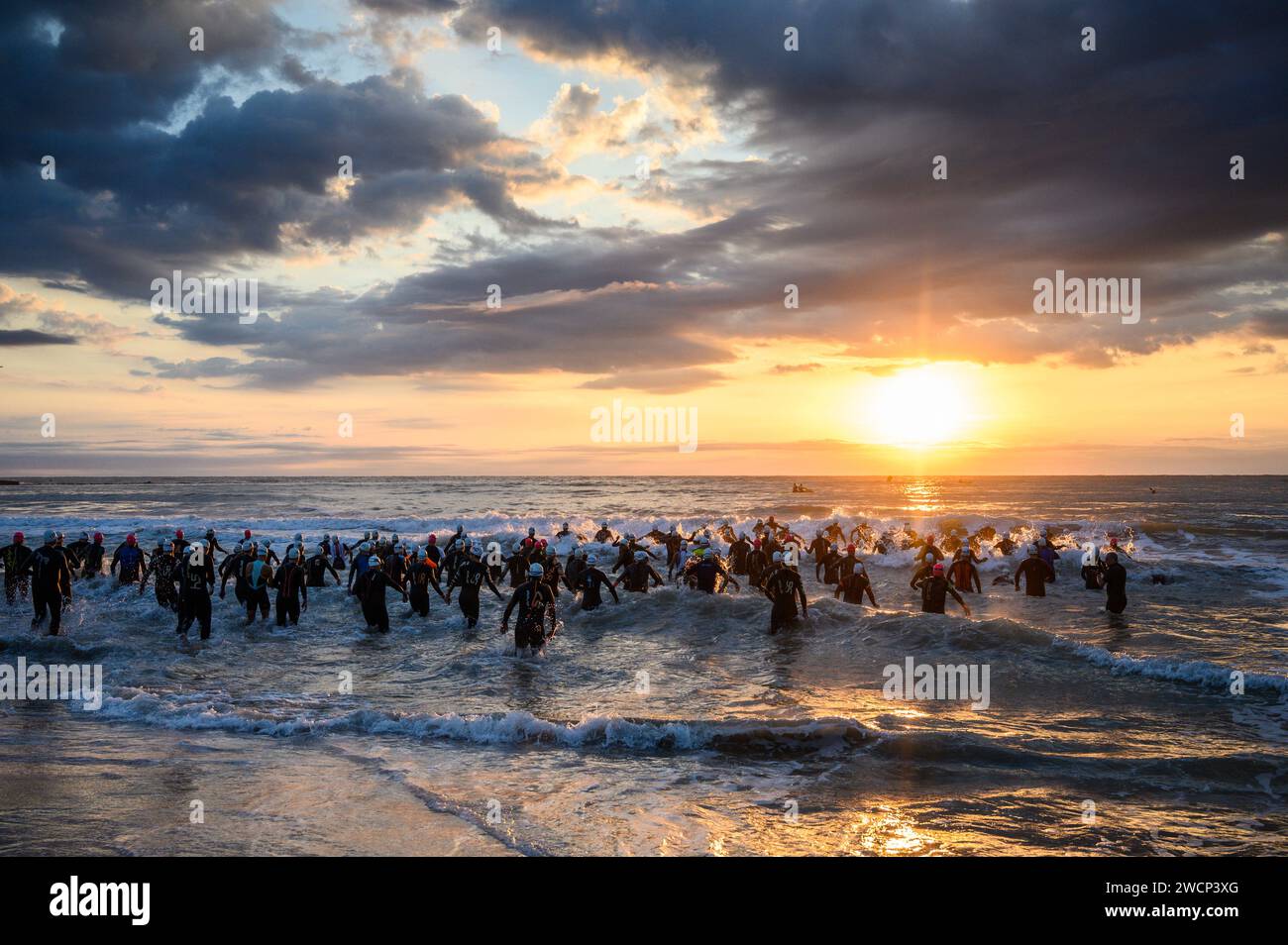 Triathletes in wetsuits running into the sea during a beautiful sunrise to start the competition in Burriana, Castellon, Spain Stock Photo